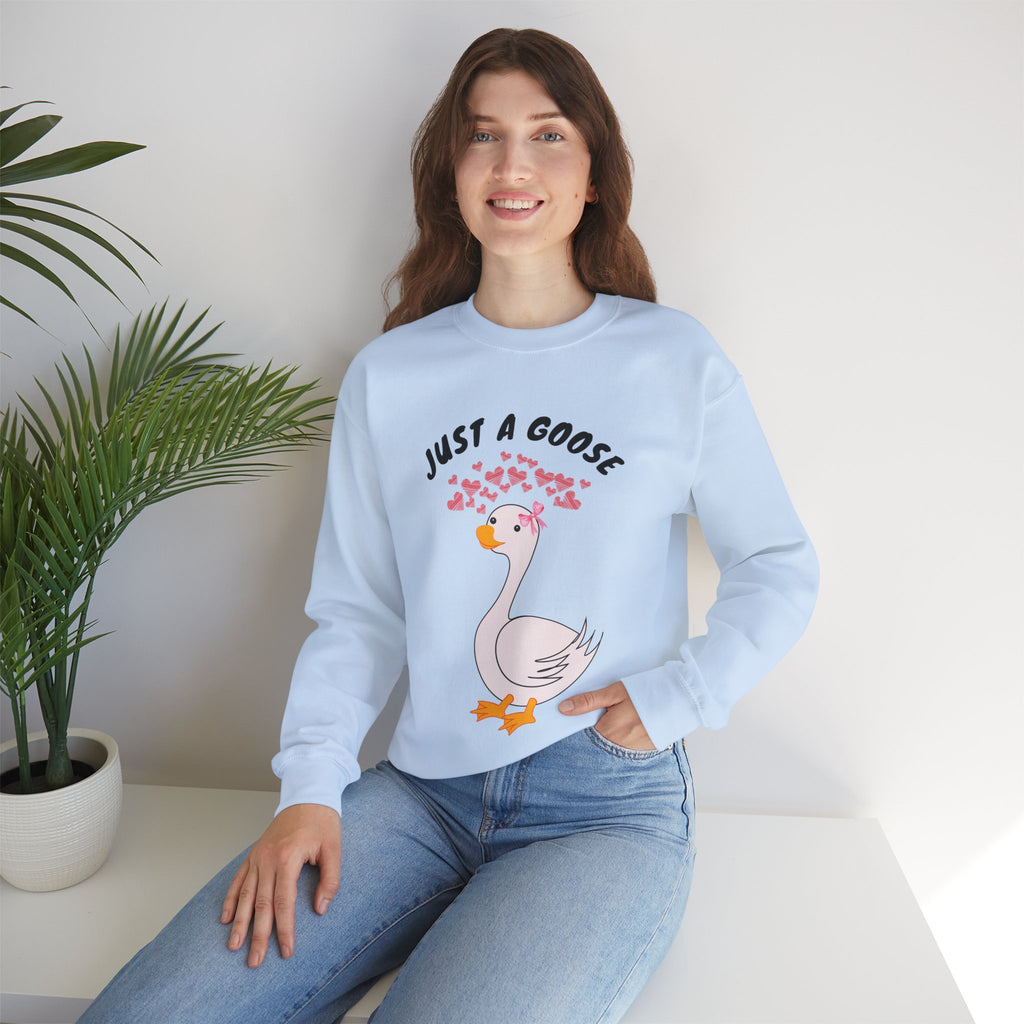 Woman wearing a light blue sweatshirt with a cartoon goose design and text, sitting on a white surface with a plant in the background.