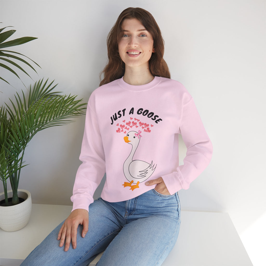 Person wearing a Light pink sweatshirt with a cartoon goose design and text, sitting on a white surface with a plant in the background.