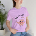 Person wearing a Heather Prism Lilac t-shirt with a cartoon cat and 'SELF CARE' text.