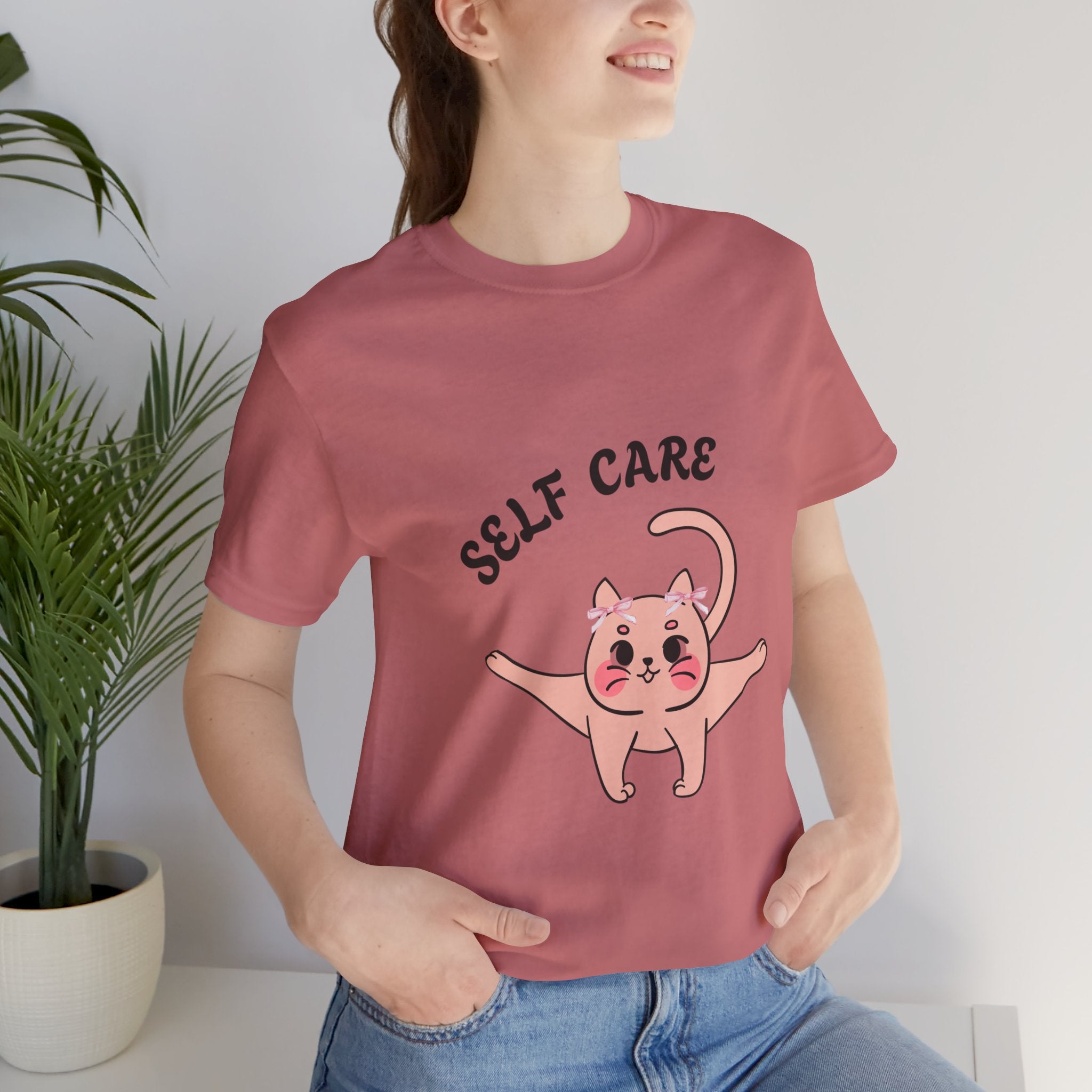 Person wearing a Mauve t-shirt with a cat illustration and 'SELF CARE' text.
