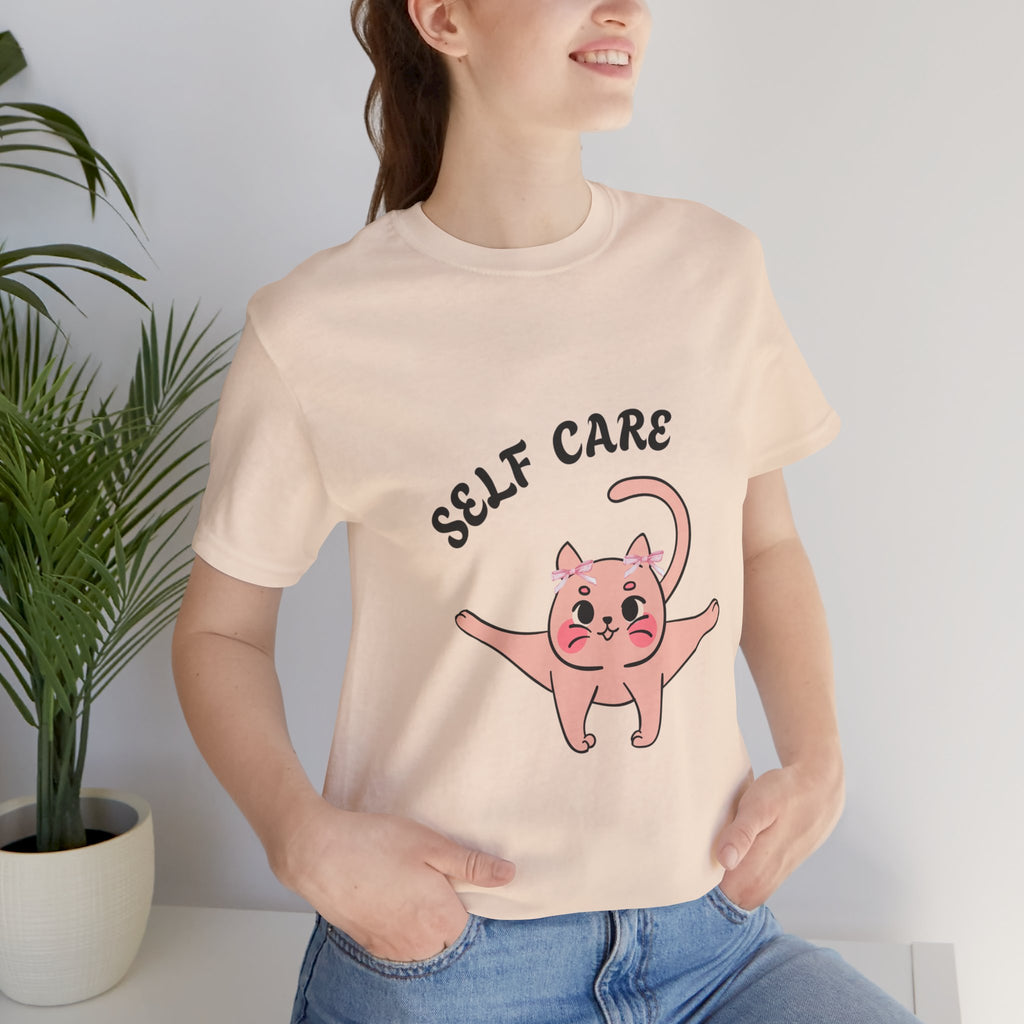 Person wearing a Soft Cream t-shirt with a cartoon cat and 'SELF CARE' text, standing indoors.