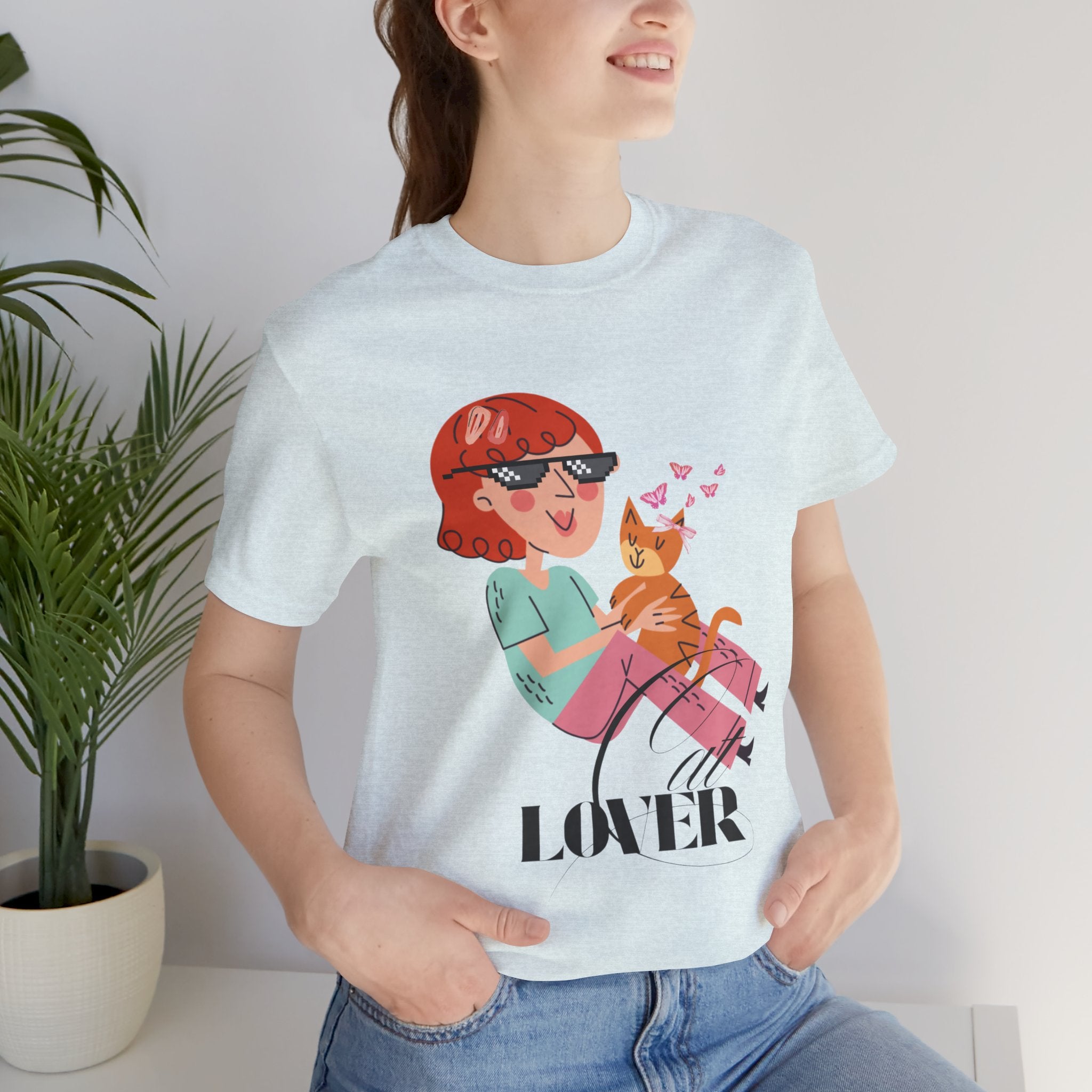Person wearing a Heather Ice Blue t-shirt with a graphic design of a woman holding a cat and the word 'LOVER'.