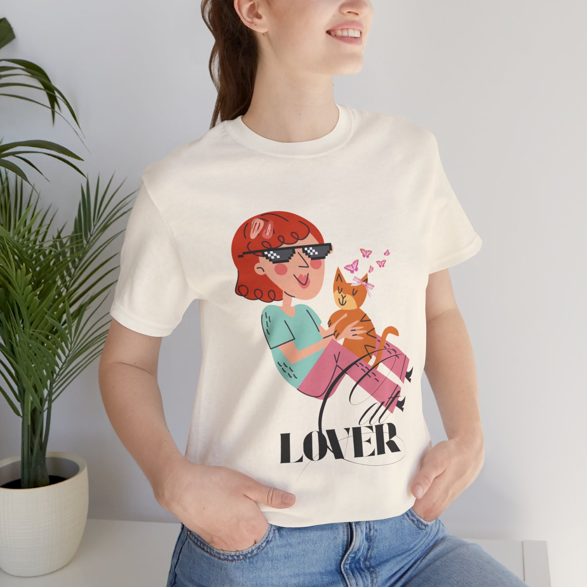 Person wearing a Natural t-shirt with a graphic design of a person holding a cat and the word 'Cat LOVER'.