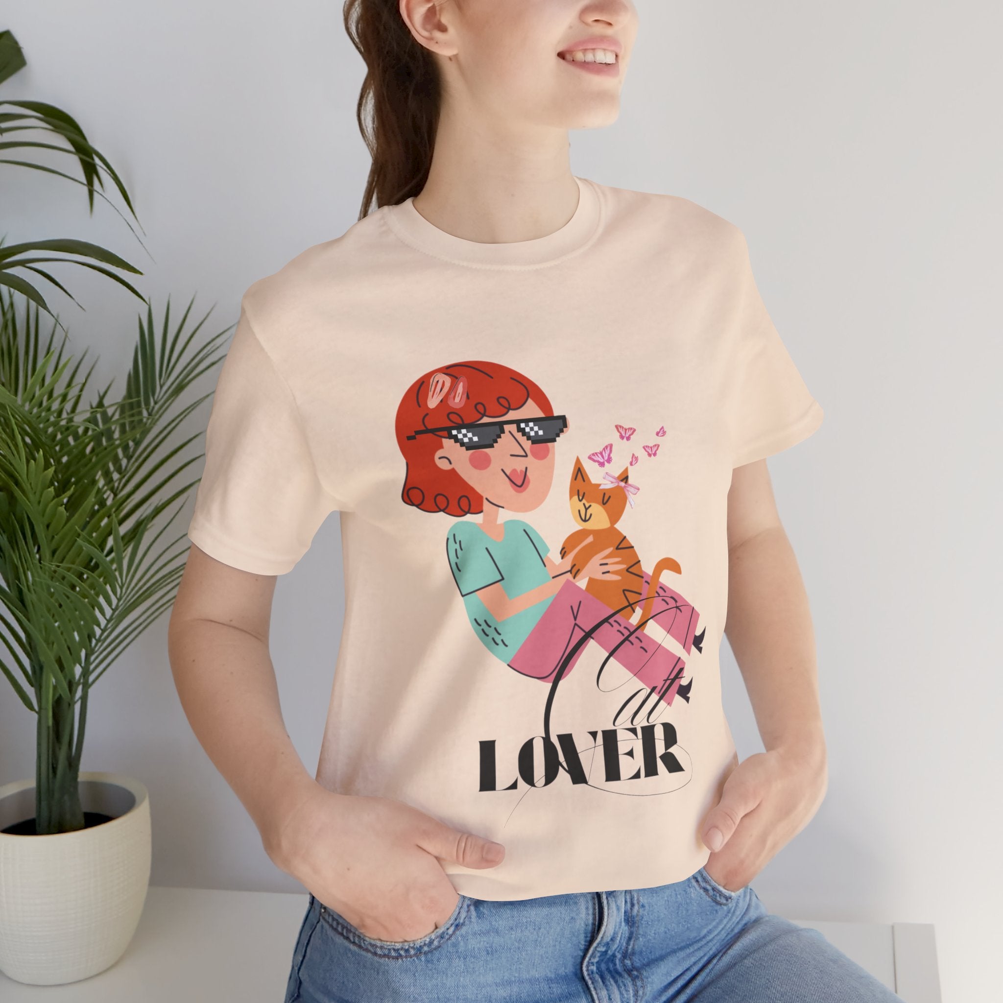 Person wearing a Soft Cream t-shirt with a graphic design of a person holding a cat and the word 'Cat LOVER'.