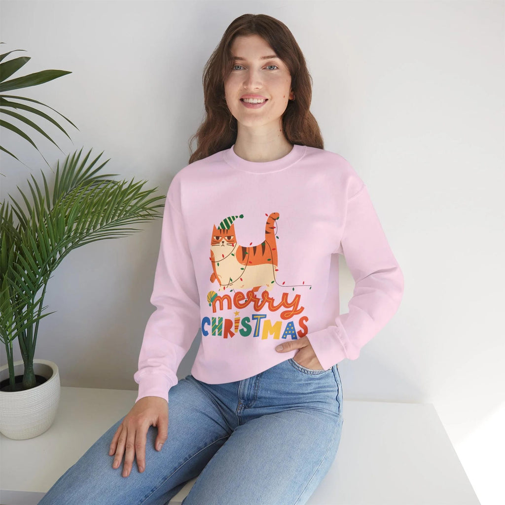 Person wearing a pink 'Merry Christmas' sweater with a cat design, sitting on a white surface with a plant in the background.