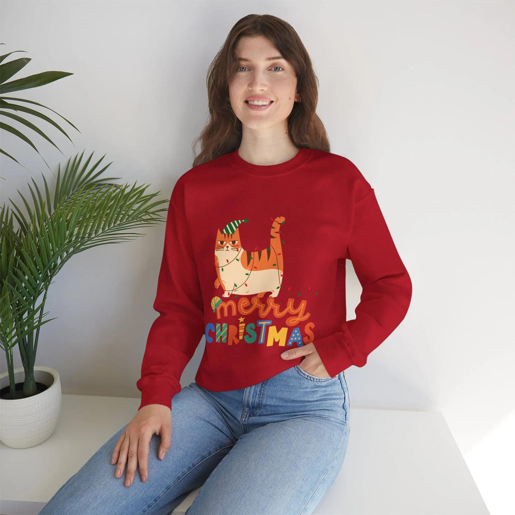Person wearing a red 'Merry Christmas' sweater with a cat design, sitting on a white surface with a plant in the background.