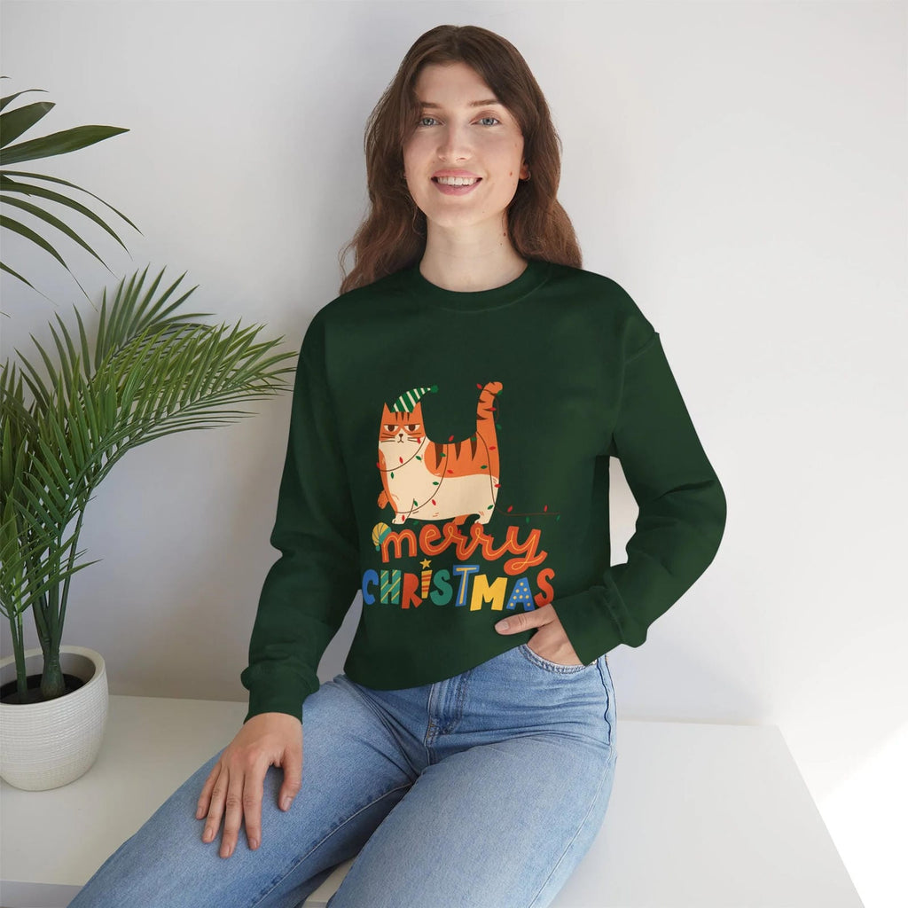 Person wearing a green 'Merry Christmas' sweater with a cat design, sitting on a white surface with a plant in the background.
