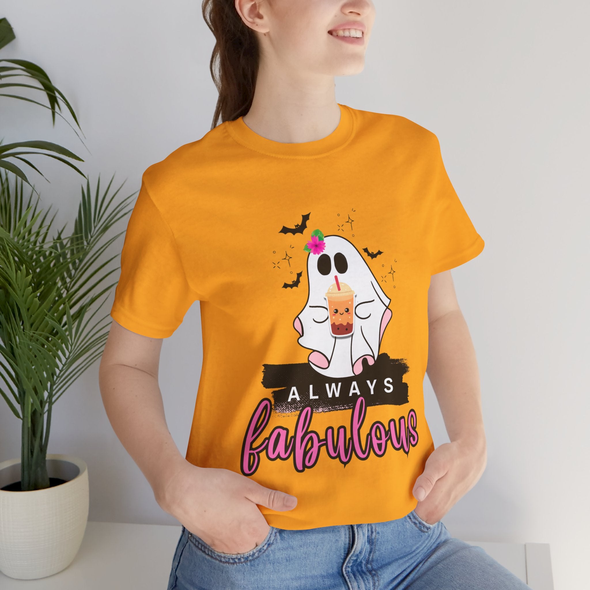 Person wearing a gold t-shirt with a ghost graphic and text, standing indoors.