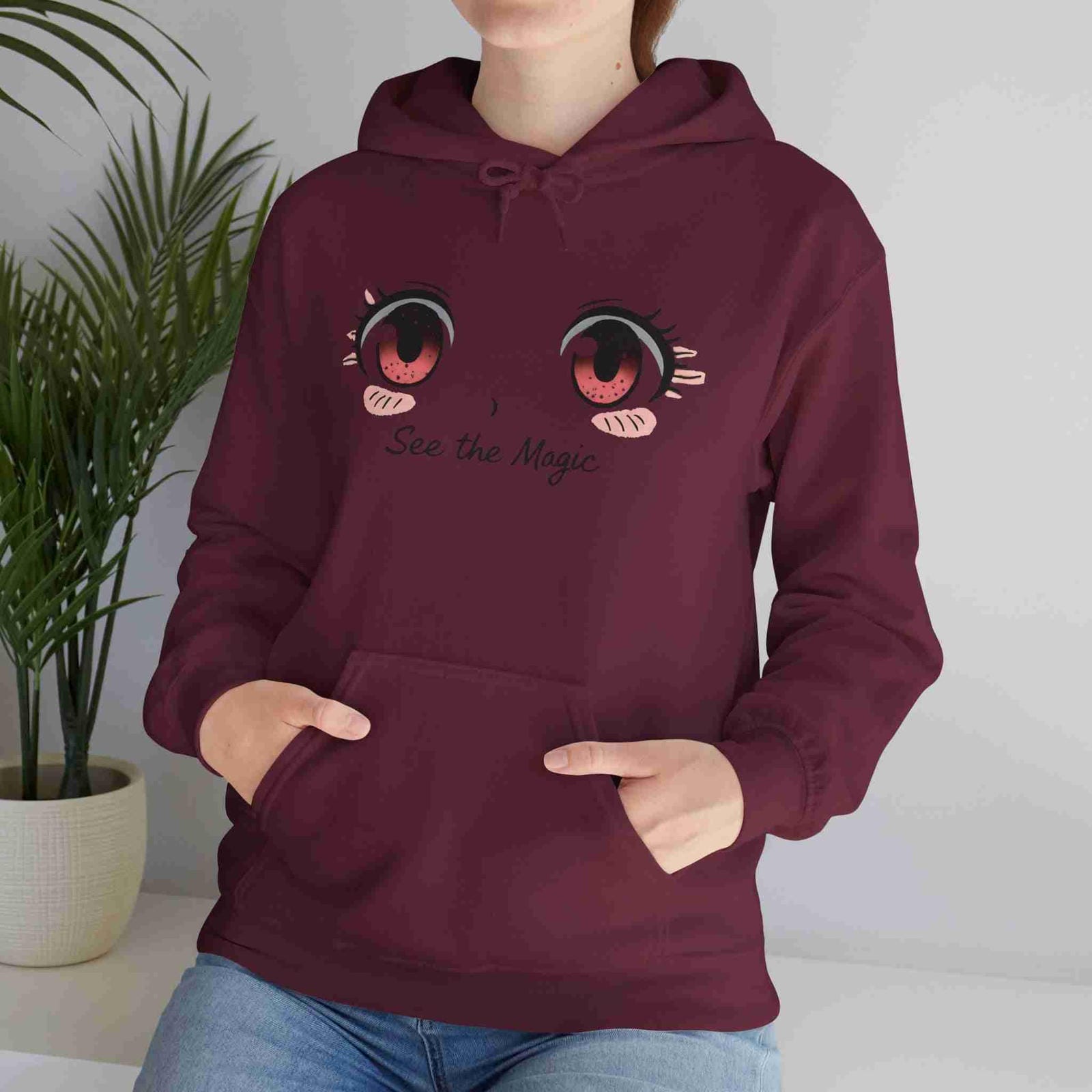 Person wearing a maroon hoodie with cartoon eyes and 'See the Magic' text, standing indoors.