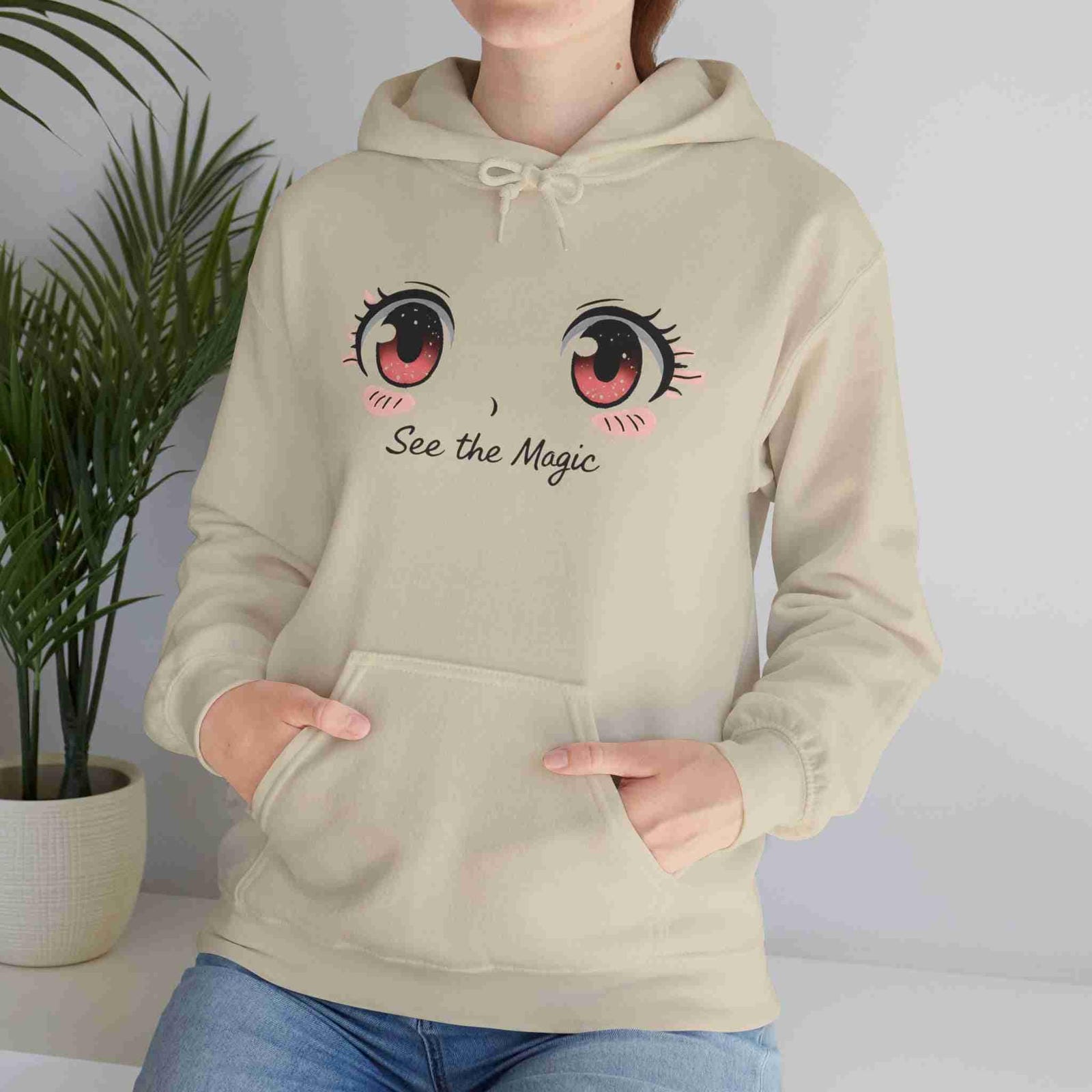 Sand hoodie with cartoon eyes and 'See the Magic' text worn by a person, against a neutral background.