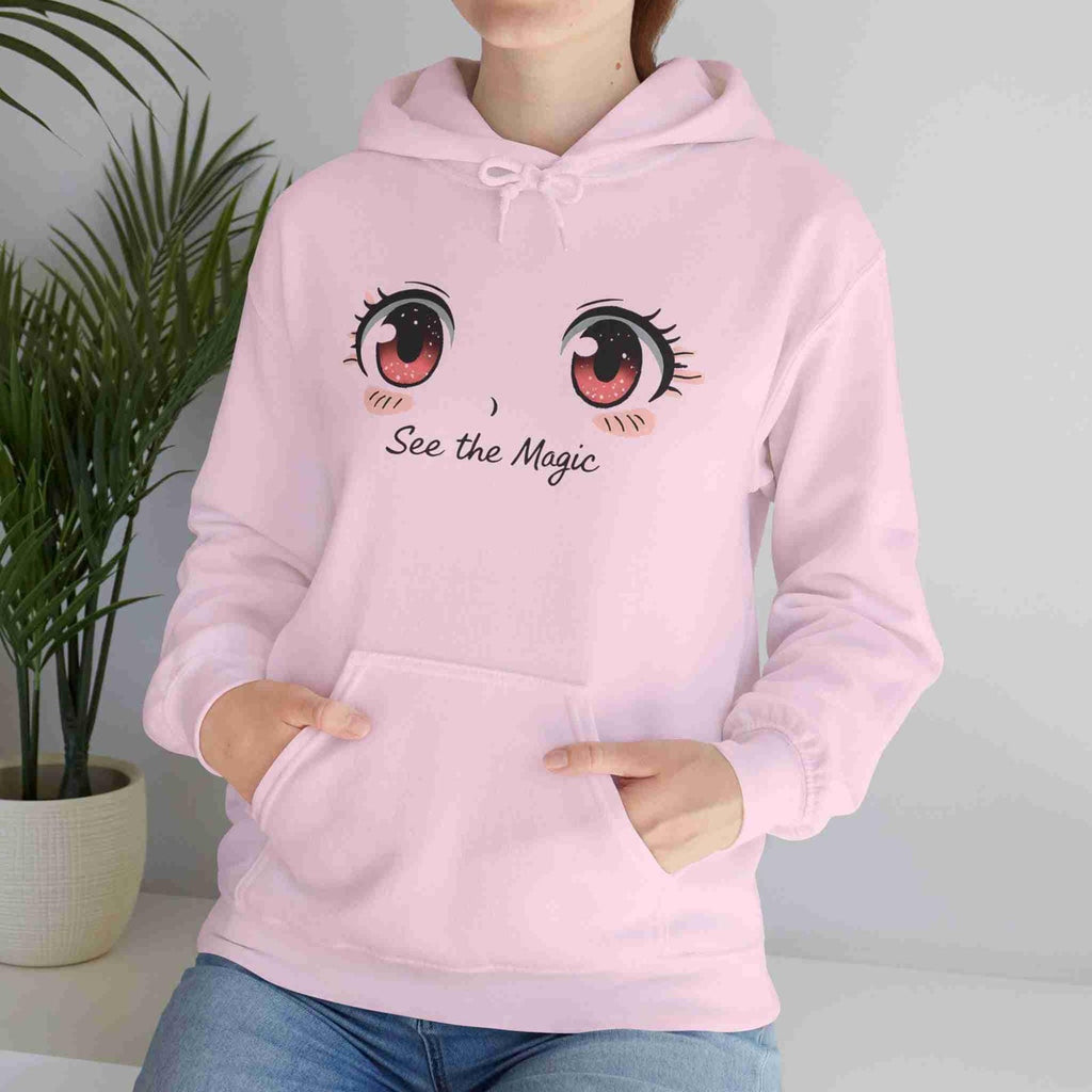Person wearing a light pink hoodie with cartoon eyes and 'See the Magic' text, standing next to a plant.