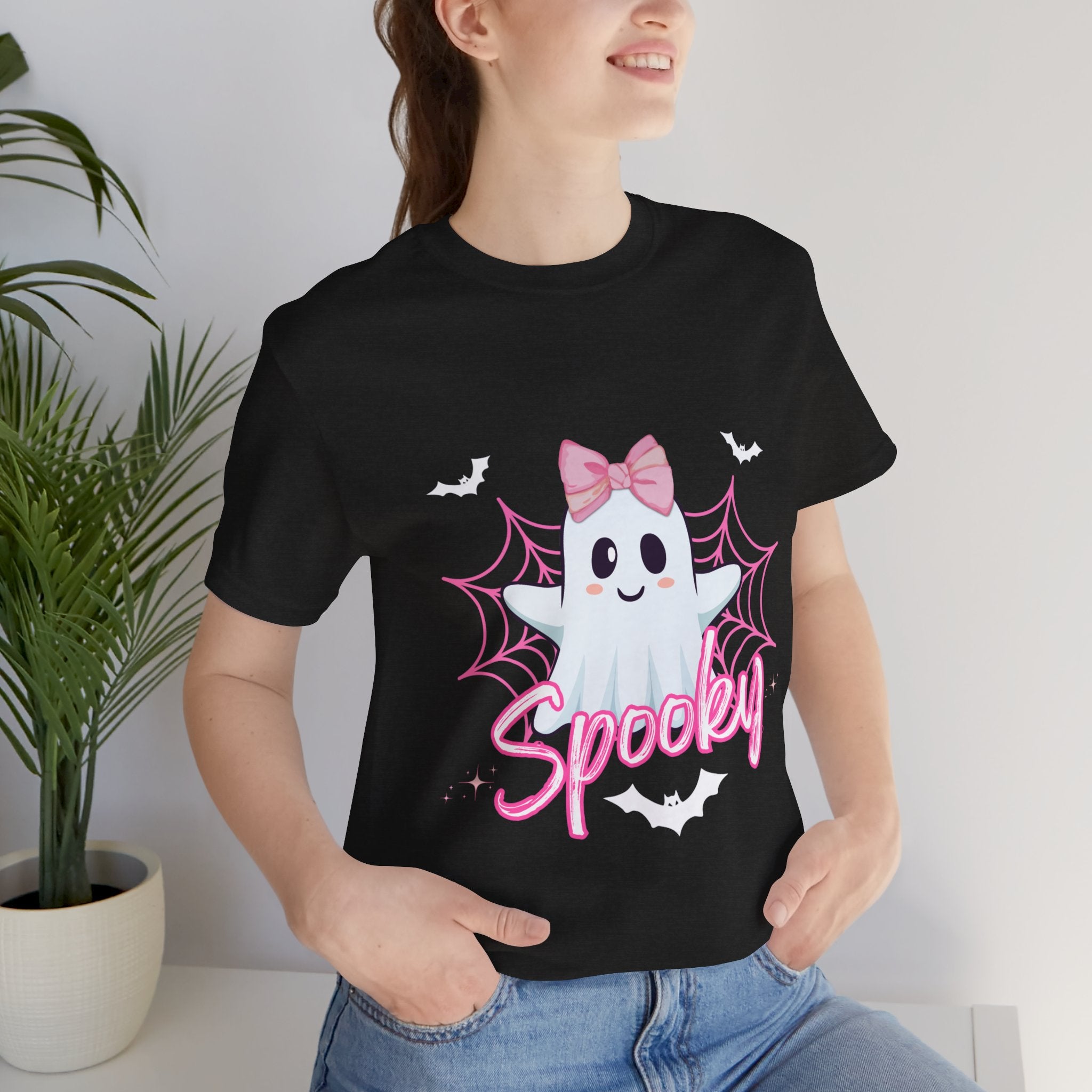 Person wearing a Heather black t-shirt with a ghost design and 'Spooky' text, standing indoors.