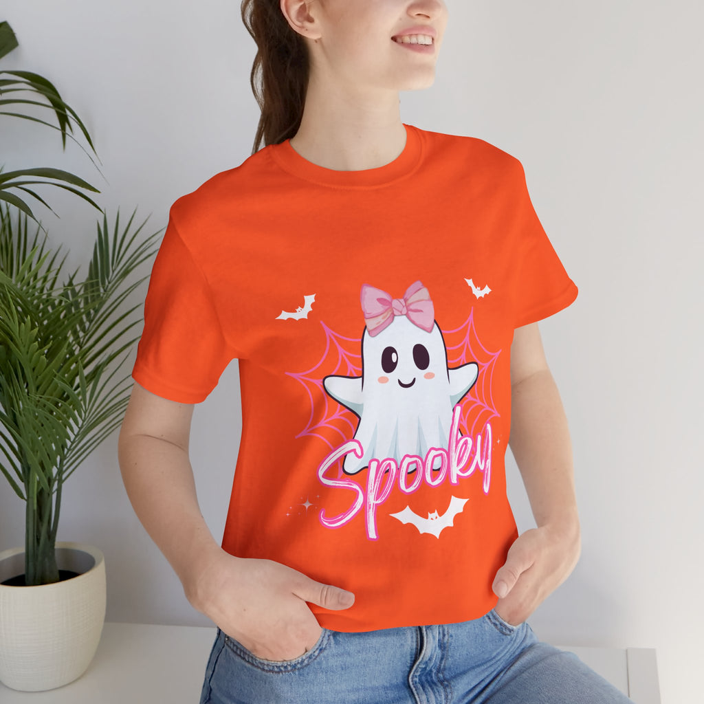 Person wearing an orange t-shirt with a ghost graphic and 'Spooky' text, standing against a white wall with a plant.
