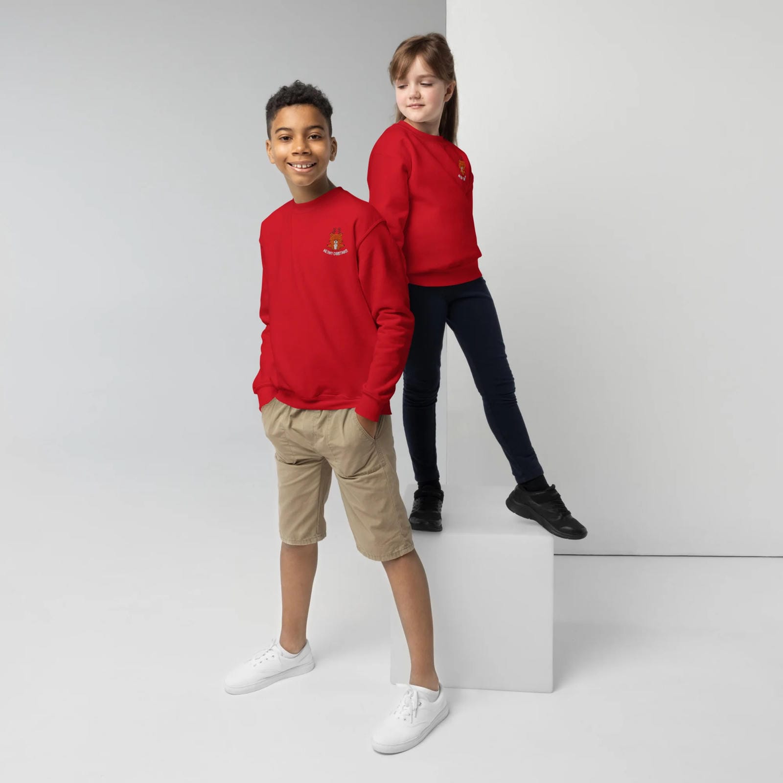 Two children wearing red sweatshirts standing on a white platform against a light gray background